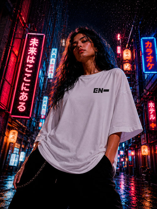 Drip&Verse white oversized 100% cotton K-Pop tee with minimalist black logo on front, worn by a woman in a neon-lit city street.