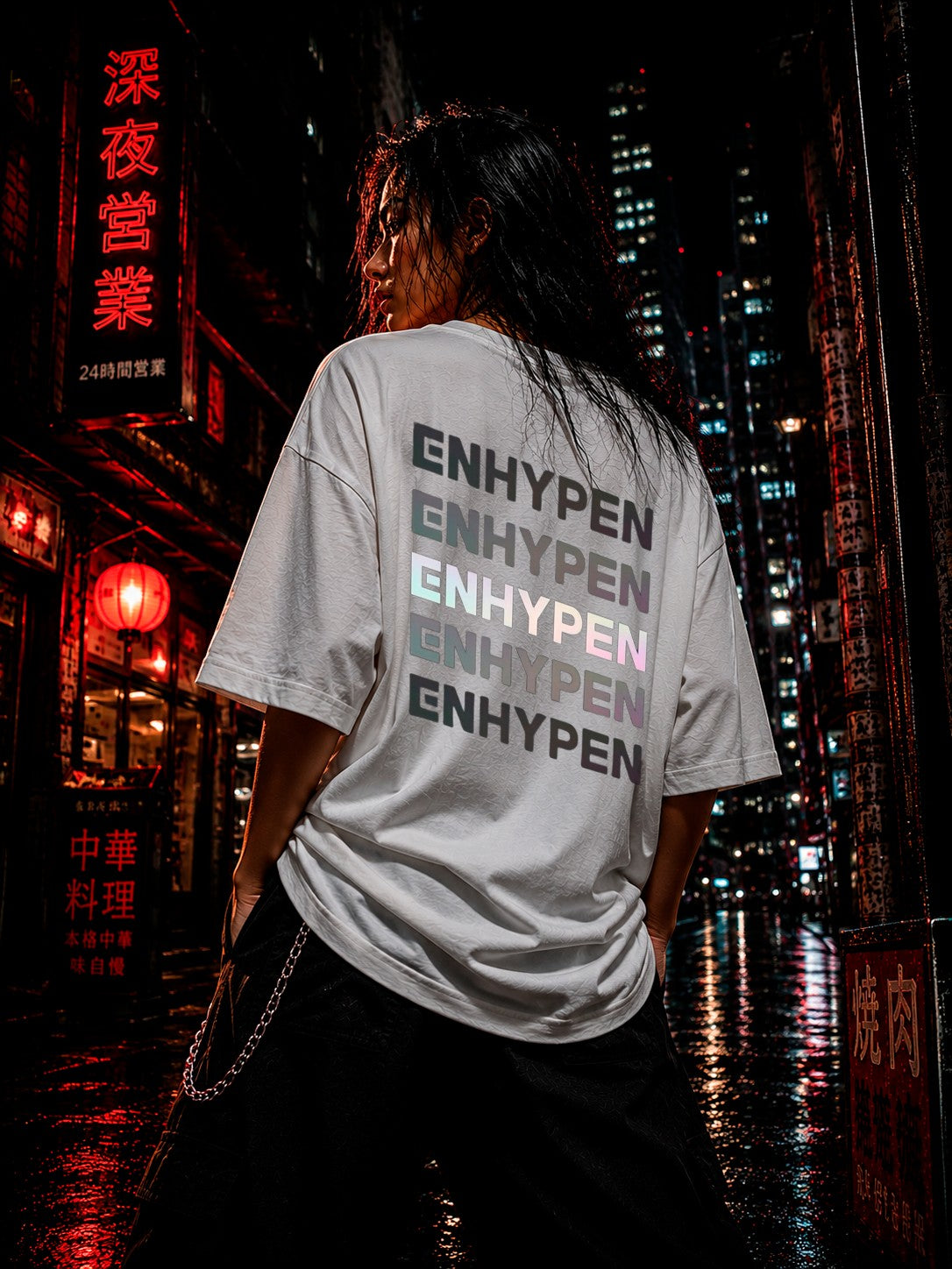 Drip&Verse white oversized cotton t-shirt with stacked holographic ENHYPEN text on back. Model in dark city setting.